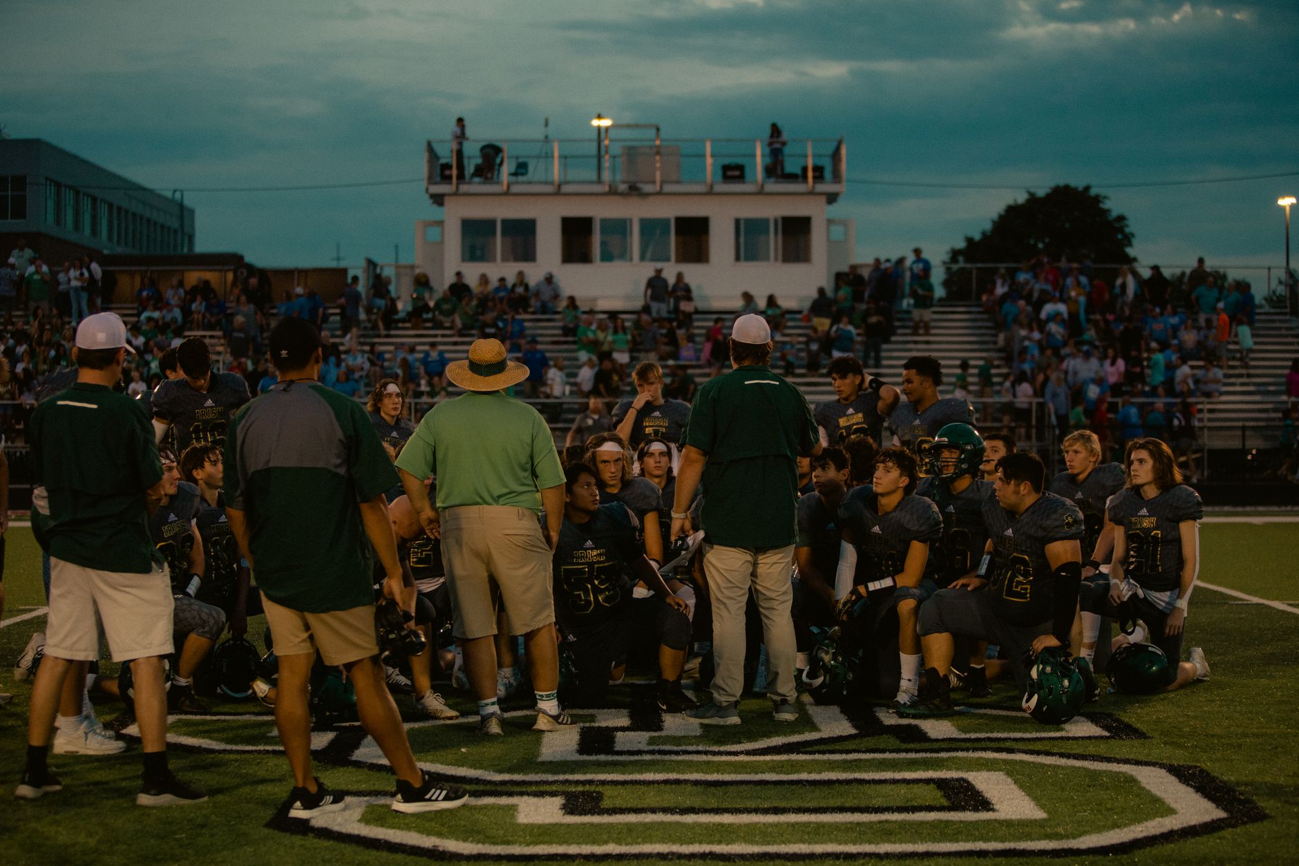 football coach leading team huddle on green field