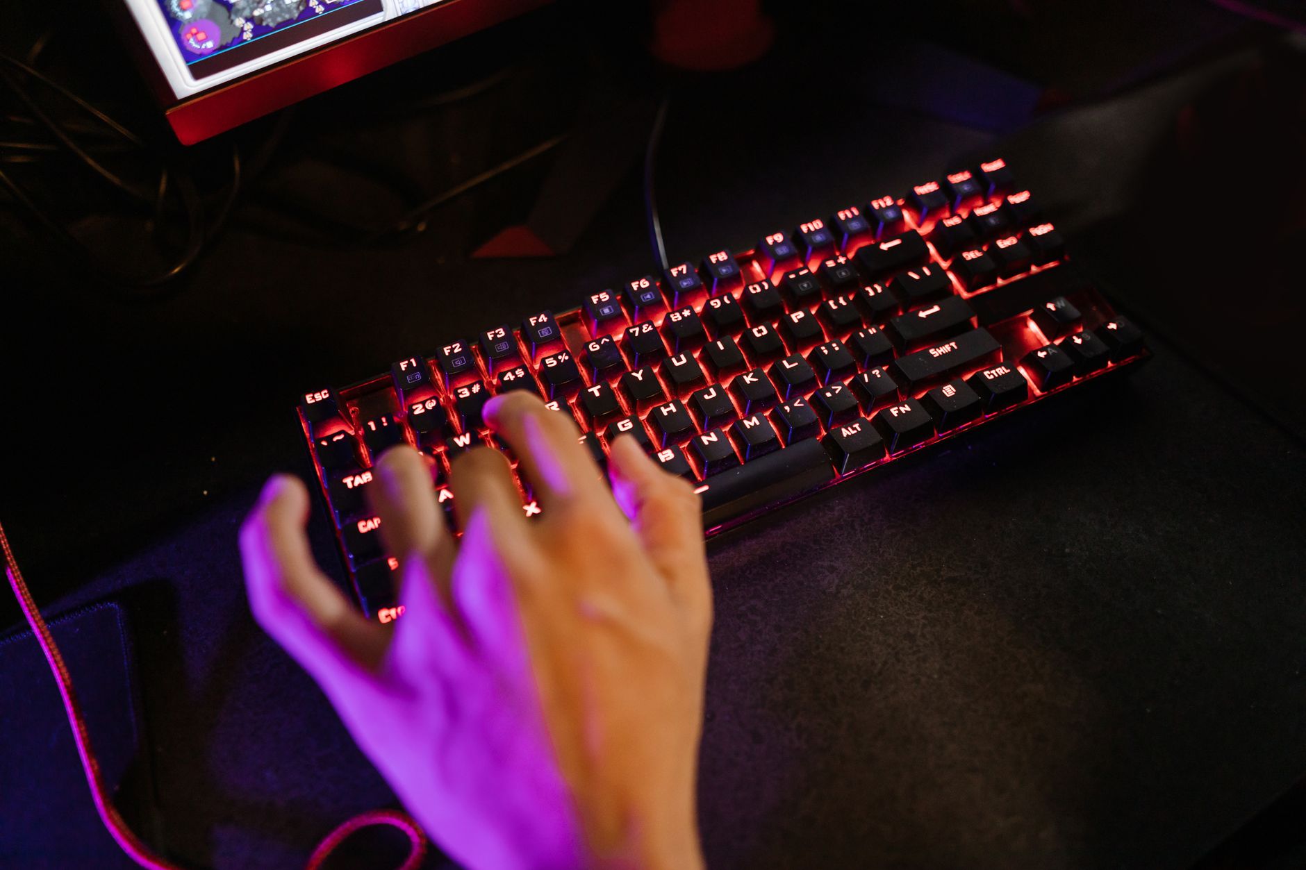 gamer hands on RGB keyboard playing game in dark room