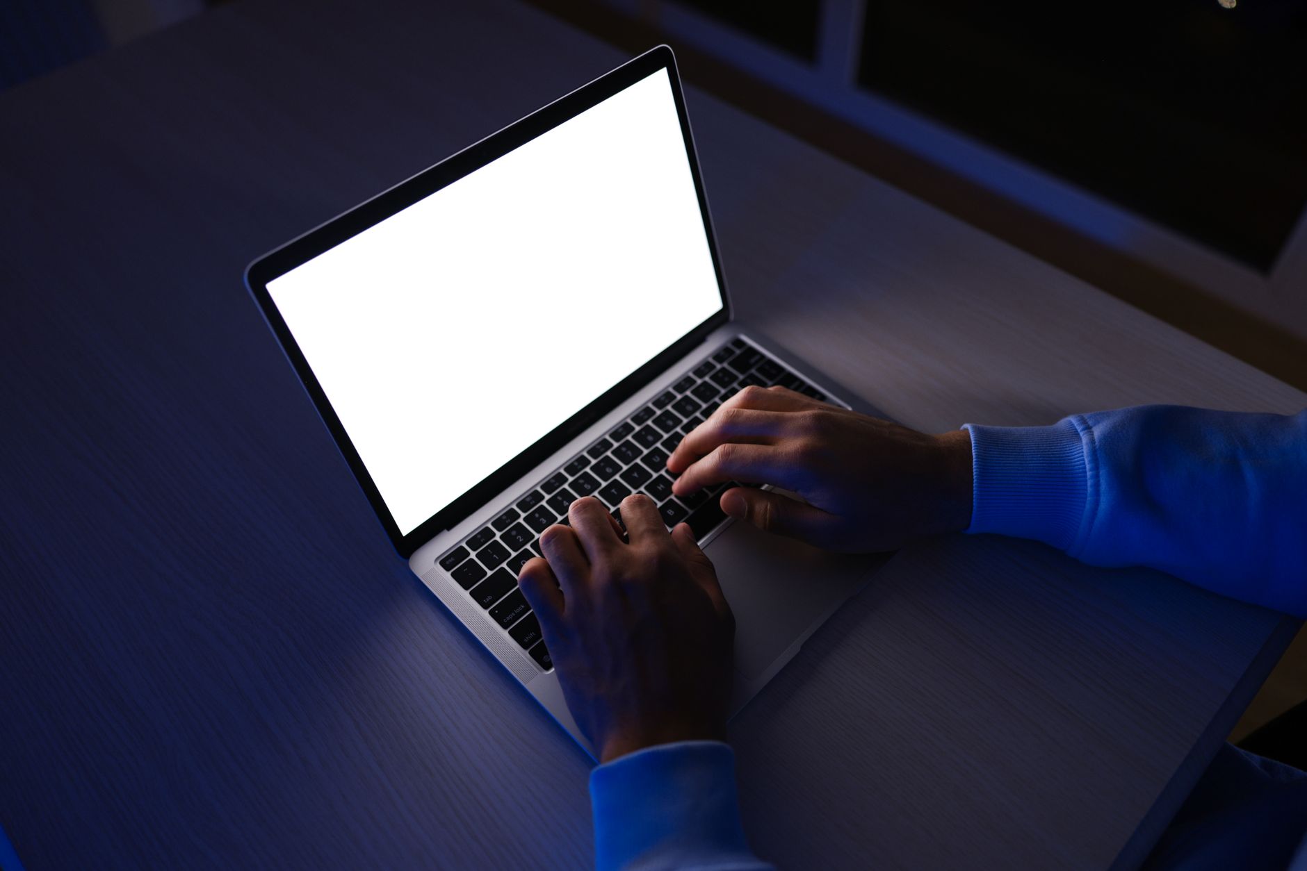 person typing on laptop keyboard in dark room