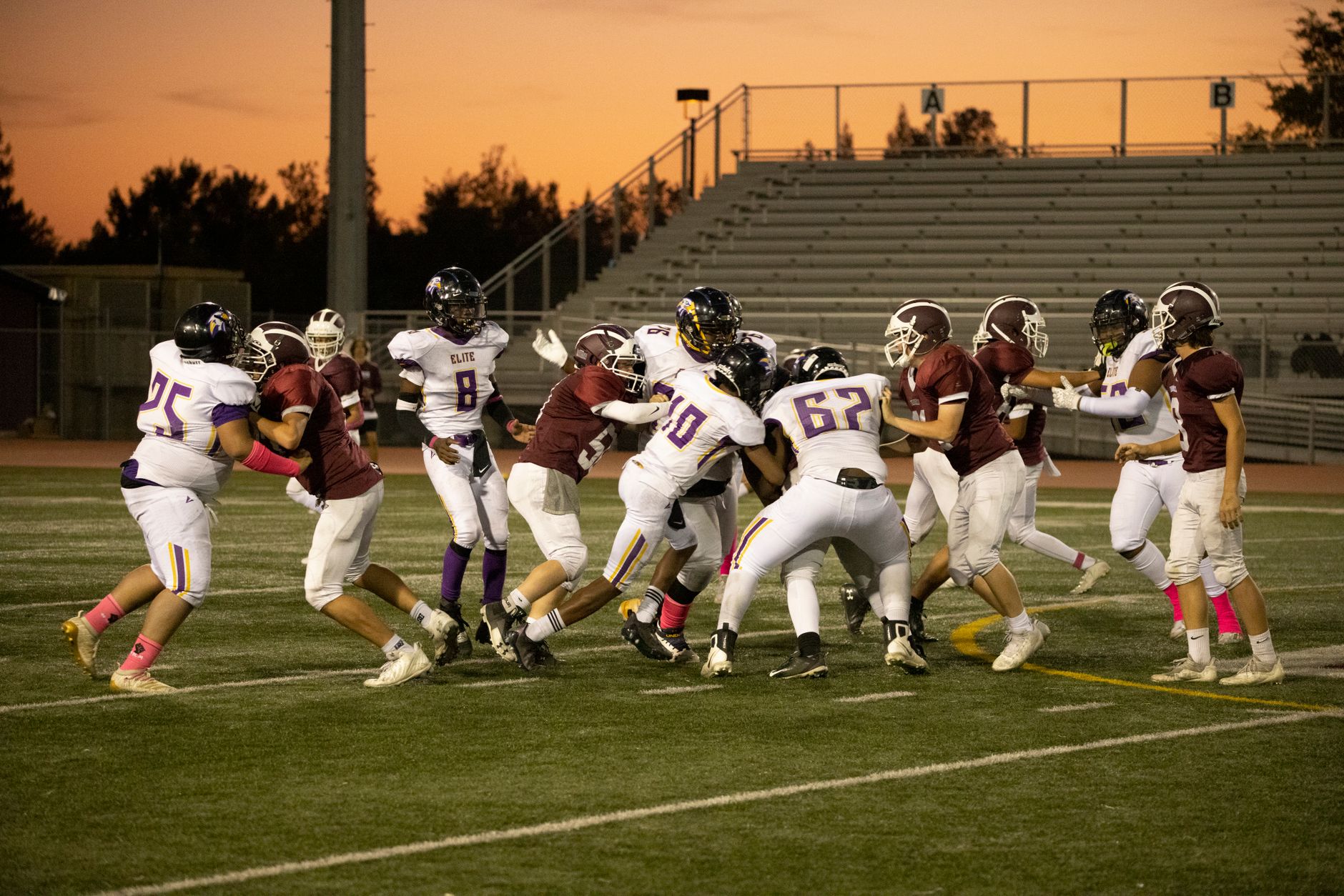 football players competing for ball on field during sunset