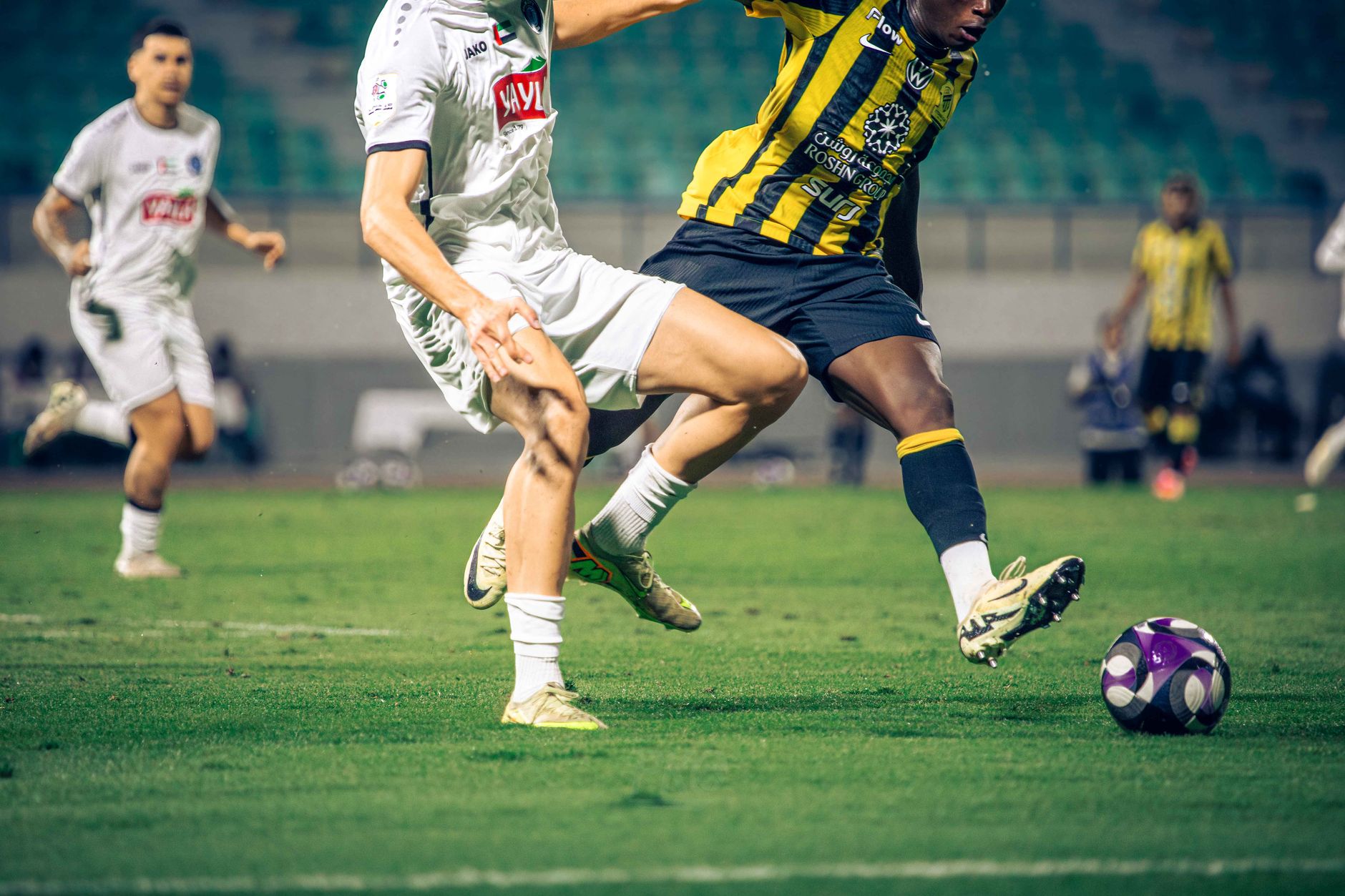 football players competing for ball on green stadium pitch