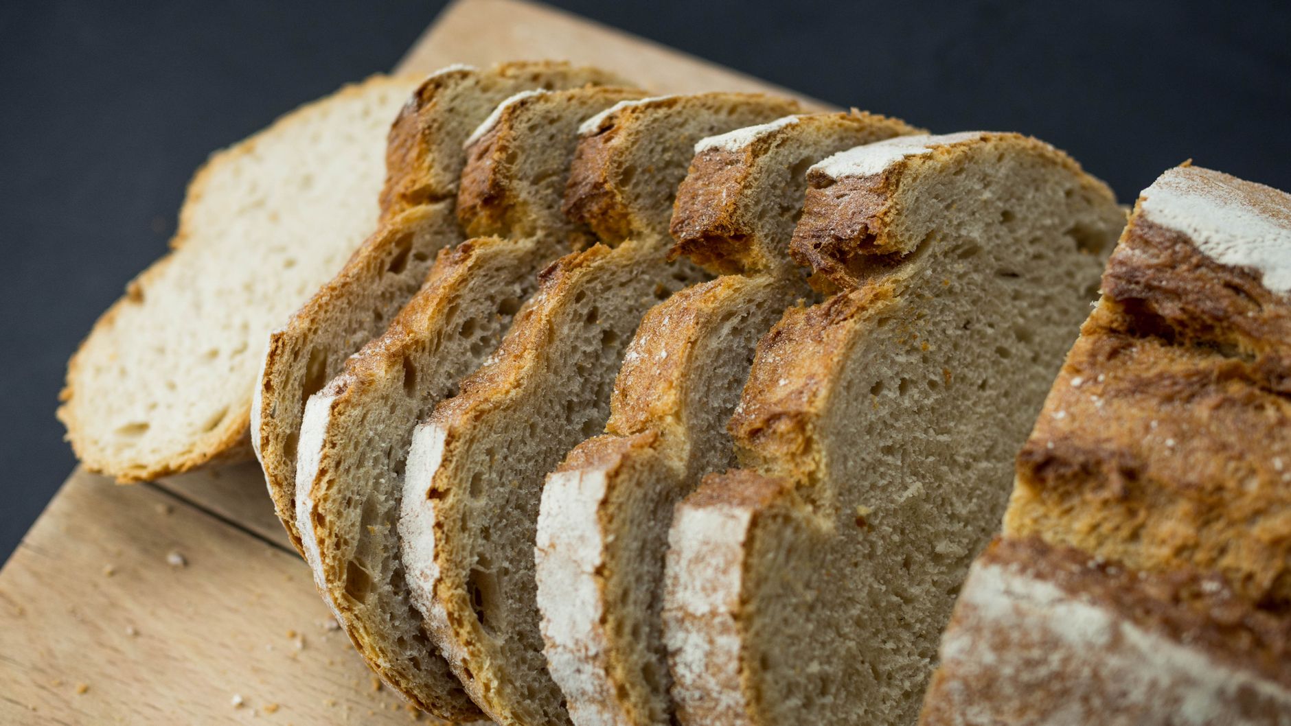 person slicing sourdough bread wooden board kitchen